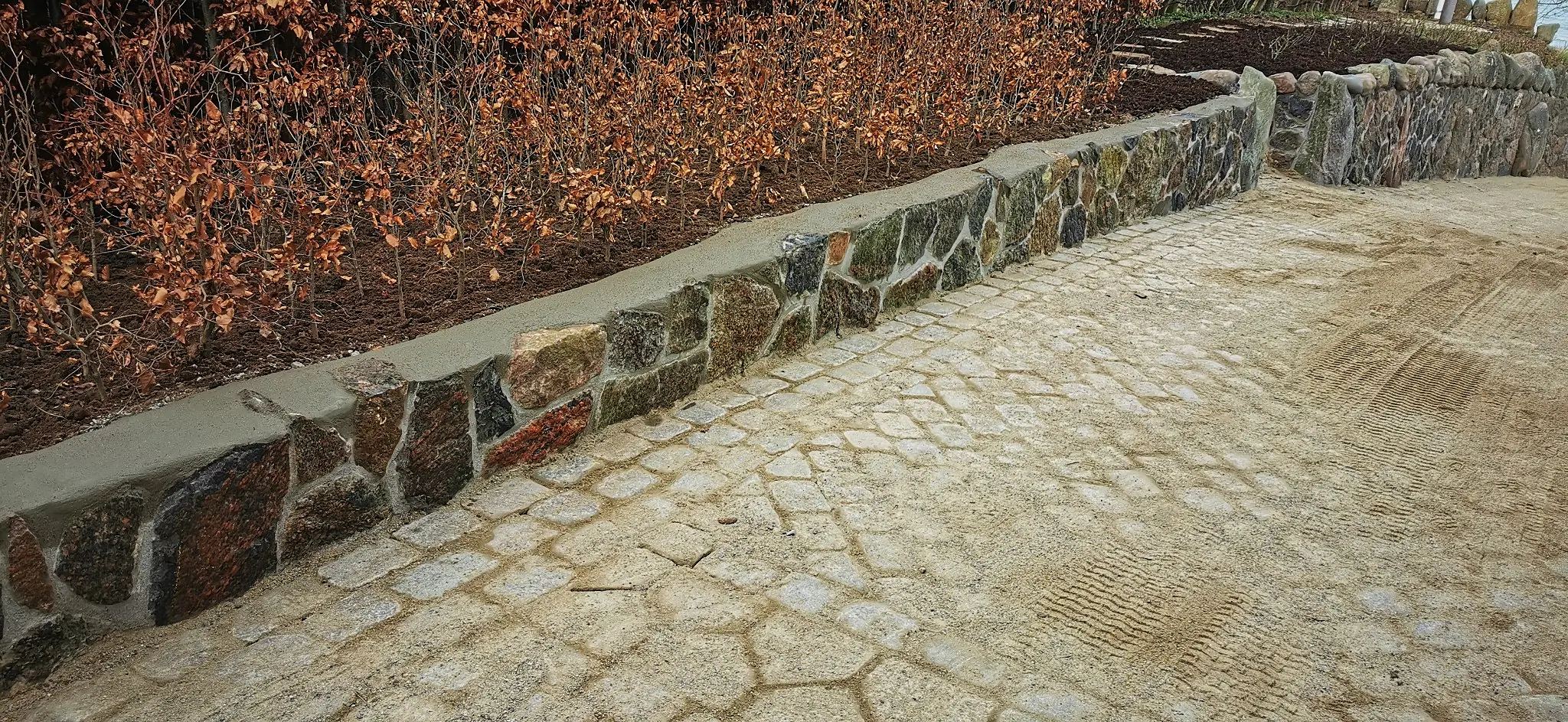 Naturstensmur langs brolagt indkørsel